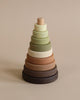 A Wooden Pyramid Stacker - Olive featuring seven rings in shades of green, beige, and brown, arranged in ascending order on a wooden base against a neutral background. This toy is coated with non-toxic paint.