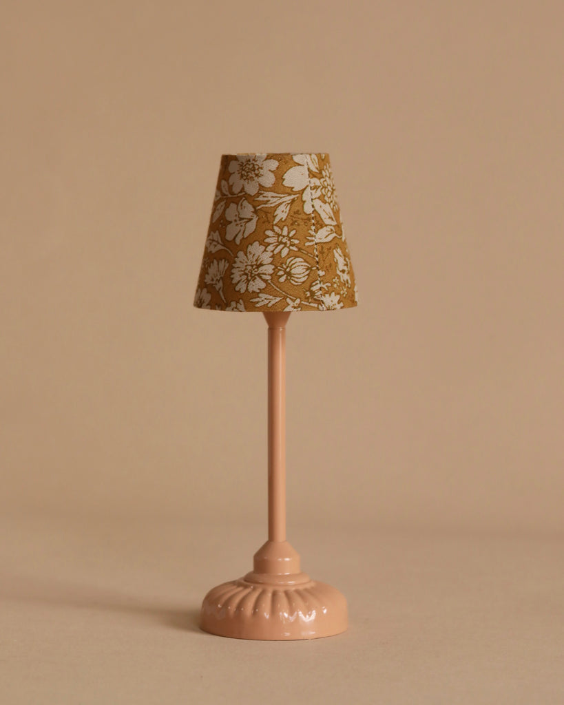 The Maileg Cozy Christmas Set features a small pink table lamp with a brown lampshade adorned with a white floral pattern, inspired by the vintage Maileg floor lamp, displayed on a beige background.