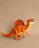 A realistic plush model of a Spinosaurus Dinosaur Stuffed Animal on a plain beige background, crafted from high-quality materials. The dinosaur model is painted in bright orange with a contrasting pattern of dark orange and black spots.