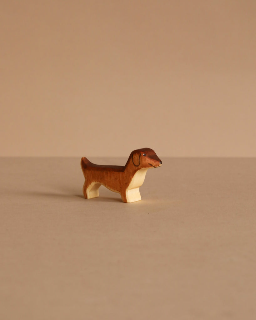 The Handmade Holzwald Dachshund Dog, Small, is a charming brown and white wooden figurine displayed on a beige surface—perfect for lovers of sustainable and classic wooden toys.