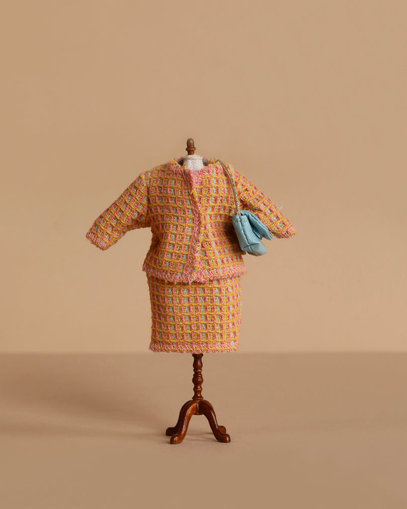 A headless, armless, and legless mannequin displays the Maileg Extra Clothing: Suit For Mom Mouse—a vibrant tweed jacket and skirt set with a light blue handbag—against a beige background. Perfect for unique doll accessory collectors.
