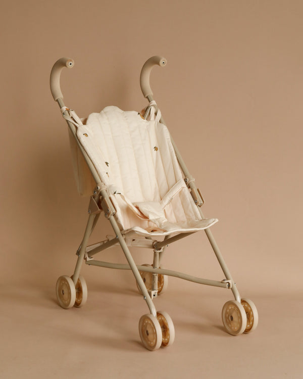 A Konges Sloejd Doll Stroller - Lemon is shown against a matching beige background. The stroller has a minimalistic design, with padded seats, curved handles, and four double wheels. The overall aesthetic is clean and elegant, blending seamlessly with the background color.