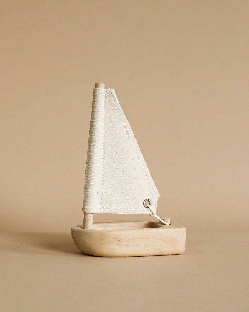 A Wooden Sailing Boat model with a textured white sail, set against a plain beige background. The boat features a minimalist design with smooth lines and a natural finish.