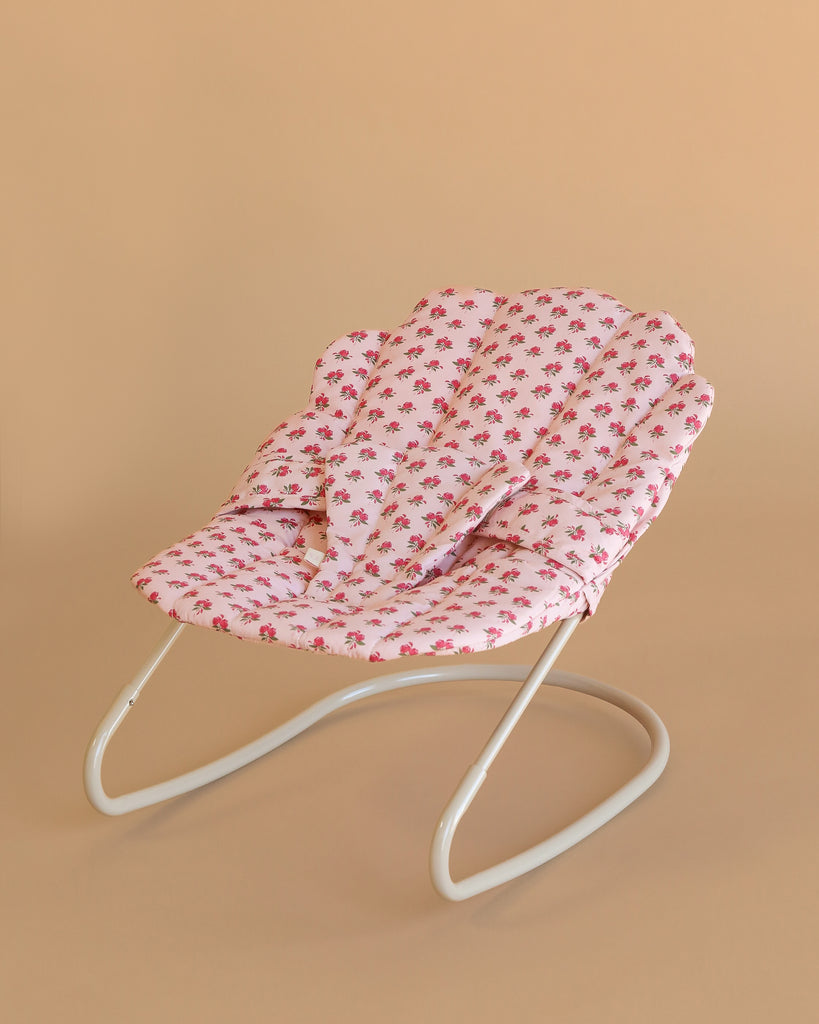 The Konges Sloejd Doll Bouncer - Rosie Rose features a white metal frame and a pink floral-patterned cushioned seat, perfect for playtime, shown against a plain beige background.