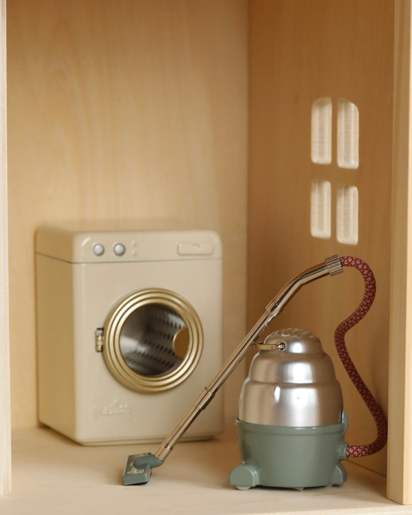Miniature models of a washing machine and a vacuum cleaner placed inside a small wooden cabinet, simulating a tidy utility closet in the Maileg Farmhouse - Fully Furnished collection.