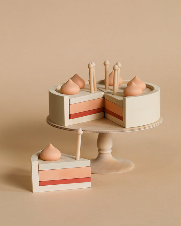 A minimalist wooden Handmade Strawberry Layer Cake On A Stand displaying toy wooden cakes and pastries, coated in non-toxic paint, arranged neatly, set against a soft beige background.