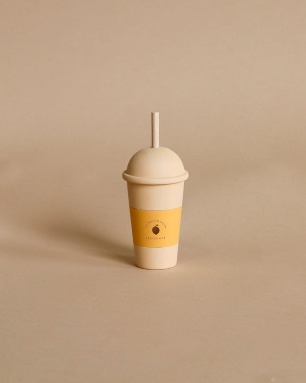 A simple, eco-friendly handmade wooden lemonade cup made in Ukraine with a lid and a straw, placed against a neutral beige background. The cup displays a minimalist sun logo with the word 'lemonade' beneath it.