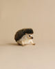 A cute Hedgehog Stuffed Animal, artisan hand sewn, with a fluffy brown and white body and black spiky back, positioned in a playful stance on a plain beige background.