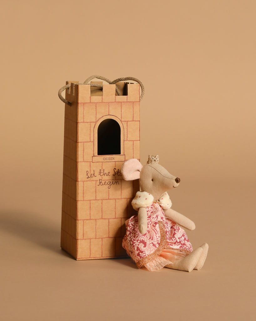 A Maileg mouse in a pink princess dress and crown sits by the Ostheimer Wooden Kingdom’s cardboard castle tower labeled “Queen” and “let the story begin”—a charming set for fans of handcrafted, whimsical toys.