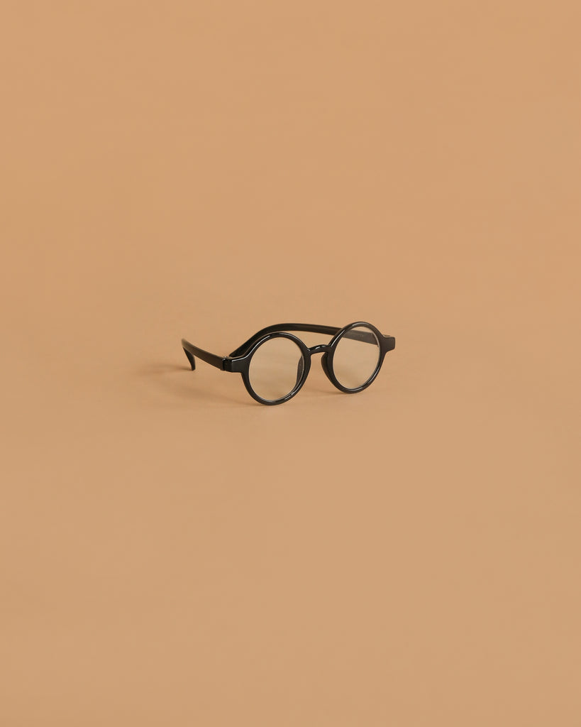 A pair of Minikane Doll Accessories Harry Sunglasses in black is centered on a plain, light brown background.