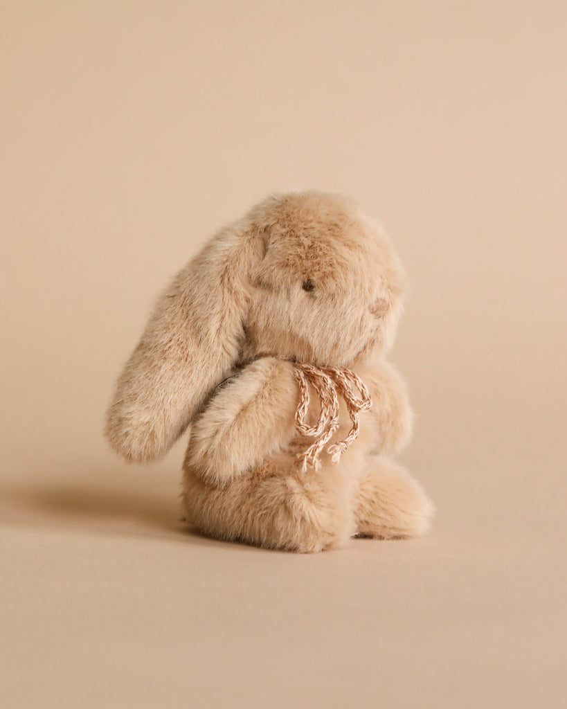 Mini plush bunny in cream peach color with bow. Photographed against beige background.
