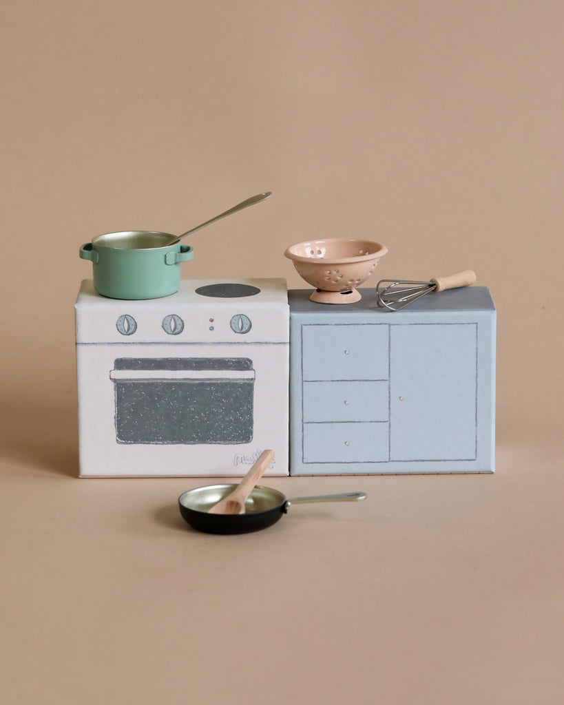 Miniature kitchen scene with a Maileg Cooking Set, including pots, a pan, and cooking utensils on a beige background.