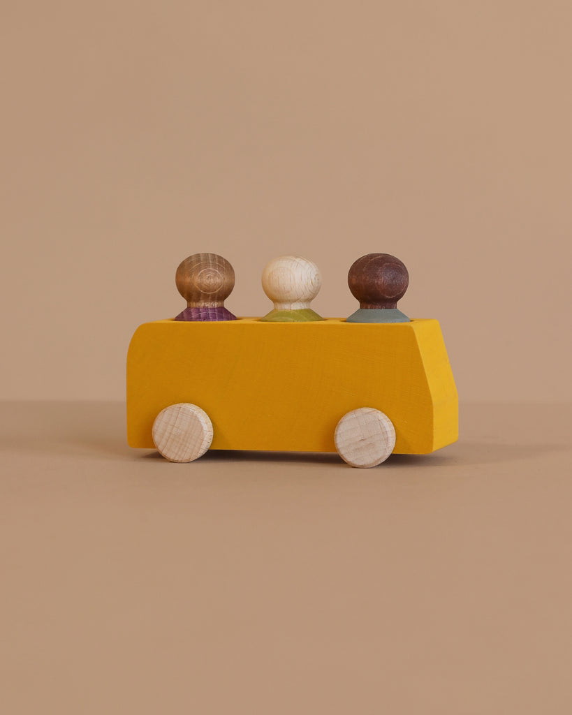 The Lubulona Wooden Bus with 3 Figures - Yellow features a minimalist yellow wooden bus and three colorful peg figures, displayed on a neutral beige background.