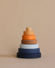 A stack of Mini Wooden Pyramid Stackers - Desert Night coated with non-toxic paint in gradient shades from dark blue at the base to light beige at the top, against a plain beige background.