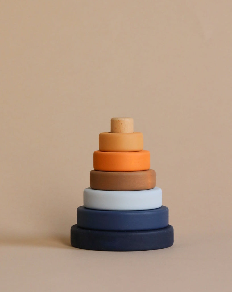 A stack of Mini Wooden Pyramid Stackers - Desert Night coated with non-toxic paint in gradient shades from dark blue at the base to light beige at the top, against a plain beige background.