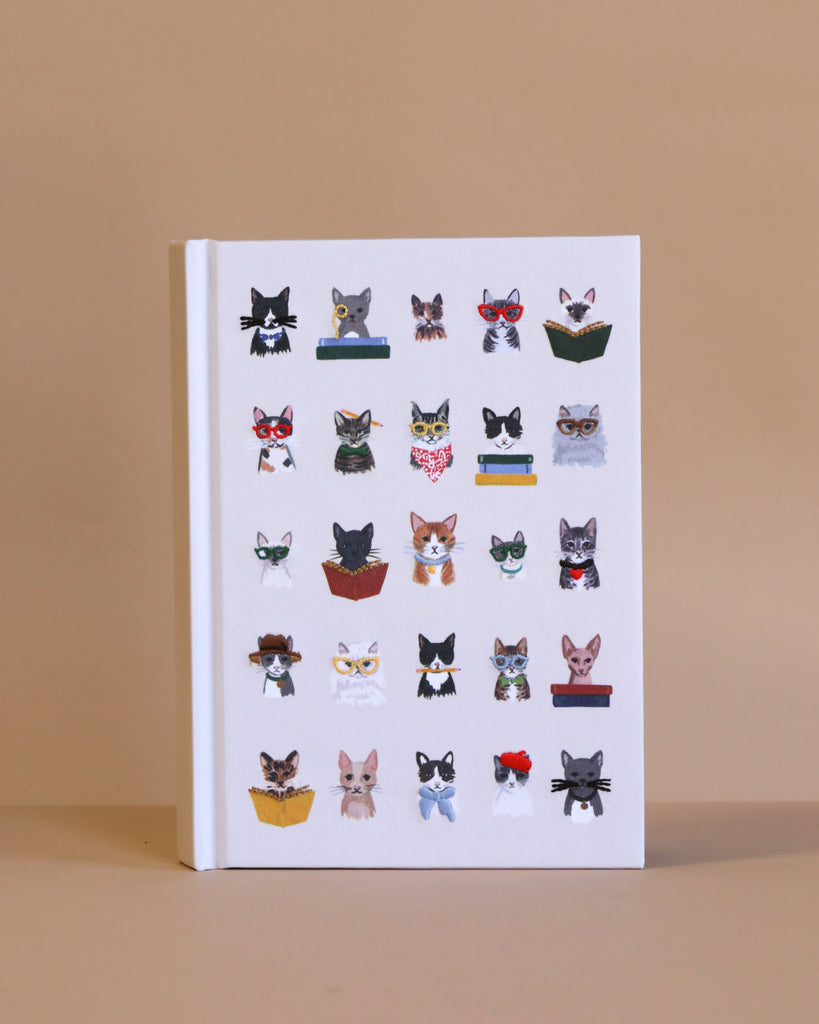 The Studious Cats Embroidered Journal features white fabric with embroidered illustrations of cats in glasses and accessories, each reading a book, arranged in a grid on a beige cover—a charming keepsake gift.