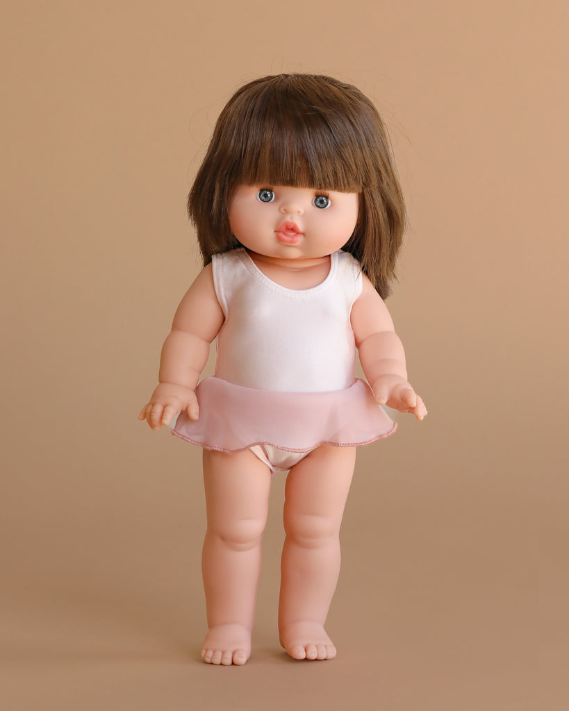 The Minikane Standing Doll (14") - Chléa With Clothing features light skin, straight brown hair, blue eyes, and stands upright in a pale pink leotard with a short skirt against a plain beige background.