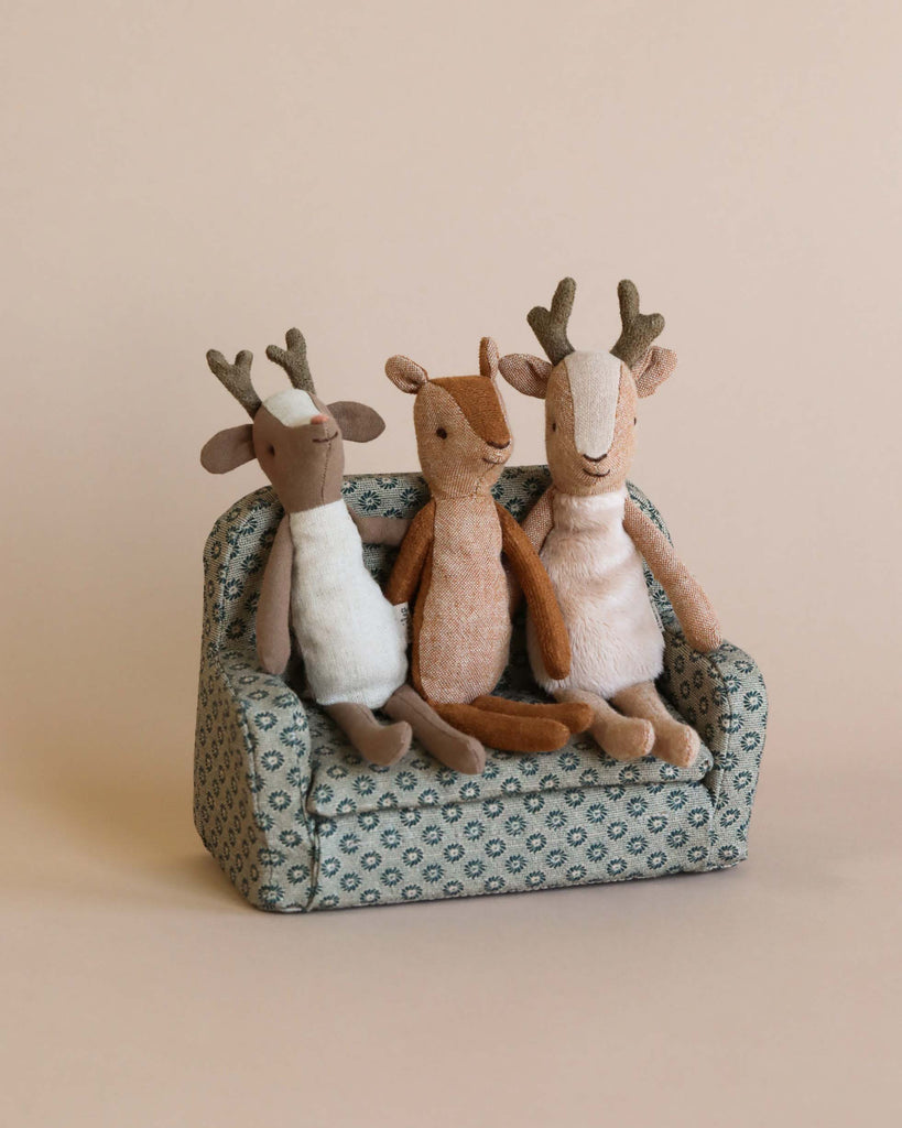 Three small deer stuffed animals sitting on a couch together.