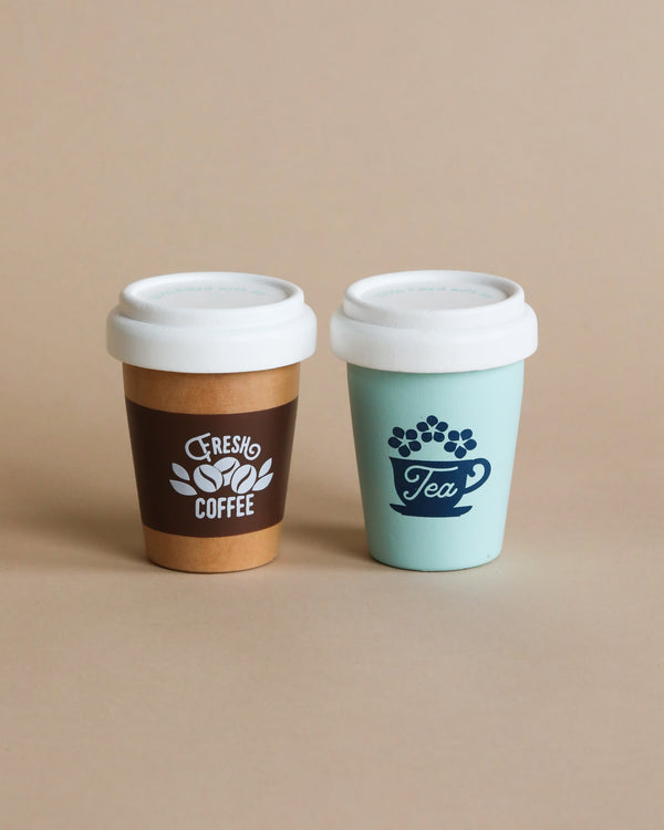 Two Wooden Coffee And Tea Cups (set) designed for children, one labeled "coffee" and the other "tea," placed against a neutral background. The coffee cup is brown and the tea cup is teal.