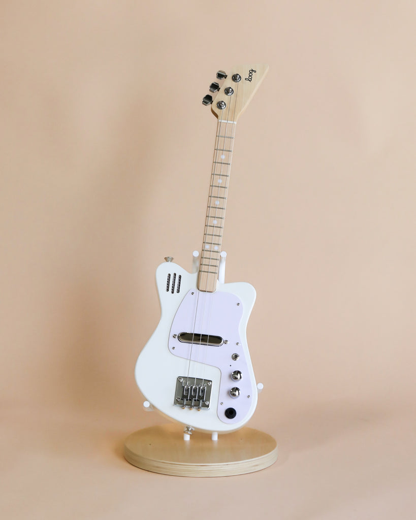 A white 3-string Electric Guitar With Strap stands upright on a rotating display stand against a light beige background. The guitar has a classic design with a glossy finish.
