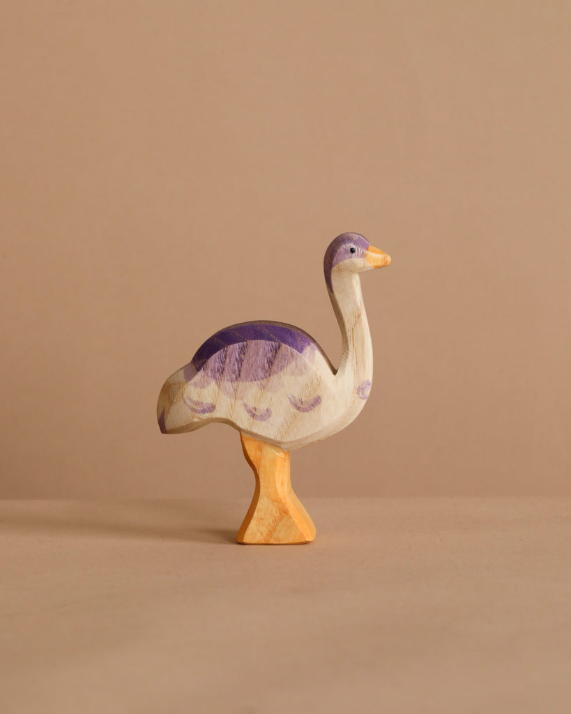 The Ostheimer Ostrich, a handcrafted wooden bird with painted purple and yellow details, stands upright on a plain beige surface, perfect for imaginative play against a matching beige background.