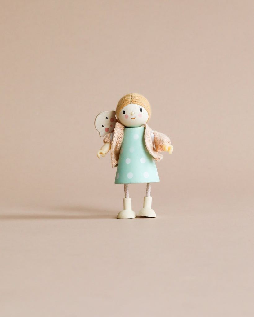 Mrs. Goodwood and her Baby, a small solid wood doll in a teal dress with polka dots and a beige scarf, holding a tiny white bear, stands against a plain light beige background.