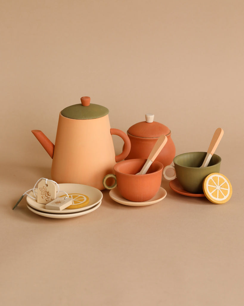 A neatly arranged Handmade Wooden Tea Set - Herbal in soft pastel colors, coated with non-toxic paint, including a teapot, cups with lemon slices, sugar bowl, and saucers on a beige background