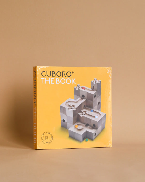 A copy of "Cuboro The Book" featuring a cover image of a 3D marble track puzzle, with marbles and wooden elements from CUBORO sets, set against a beige