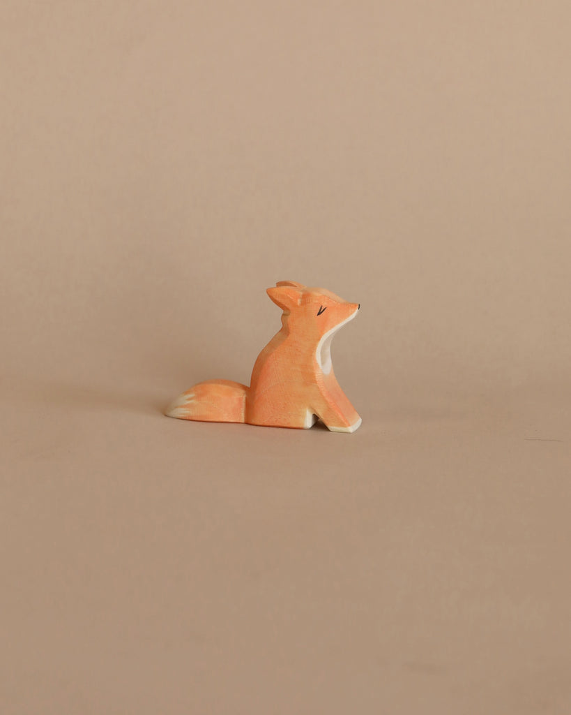 A handcrafted Ostheimer Small Fox - Sitting figurine, painted orange with white details, sitting against a plain beige background.