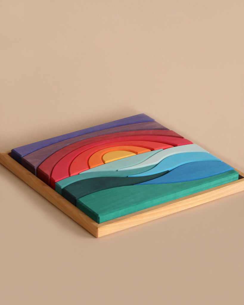 A Grimm's Creative Puzzle Landscape Block Set depicting a stylized landscape with a sunset over waves, designed to enhance fine motor skills. The pieces vary in color, including shades of purple, red, orange, yellow, blue, and green. Perfect for encouraging spatial thinking as children engage with the intricate landscape building blocks.