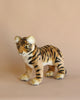 A plush toy of a Tiger Cub - Standing with realistic features, standing against a soft beige background. The tiger is positioned in a walking stance and features striking black stripes and a focused expression.