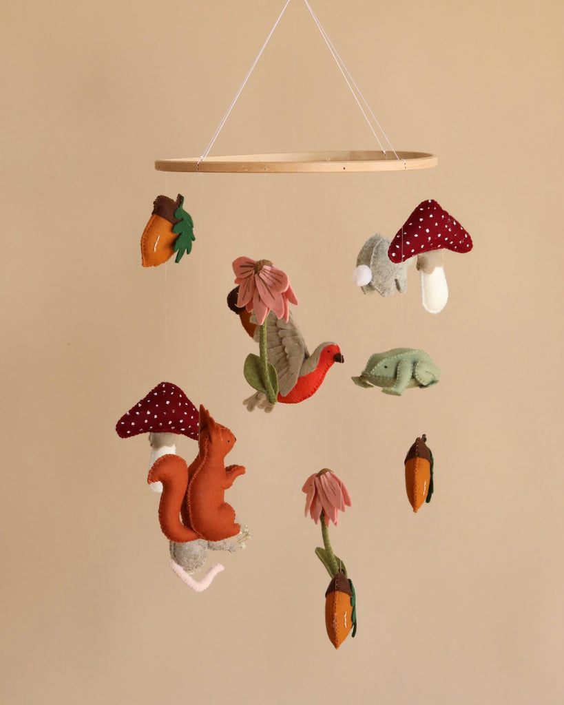 A Handmade Mobile - Forest Friends - Final Sale featuring handmade felt decorations including red mushrooms, green leaves, orange carrots, and a pink flower, suspended from a circular wooden frame.
