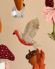A close-up of a Forest Friends handmade mobile featuring a handcrafted felt bird with detailed stitching, wings outspread, in warm earth tones, suspended among other whimsical felt elements like flowers and mushrooms.