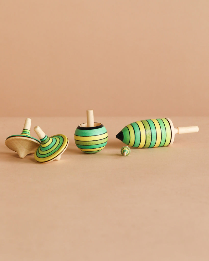The Spinning Top Champion Learning Set - Grass includes four wooden tops in different shapes and sizes with green and yellow stripes, perfect for all skill levels and adding a playful touch to any room.