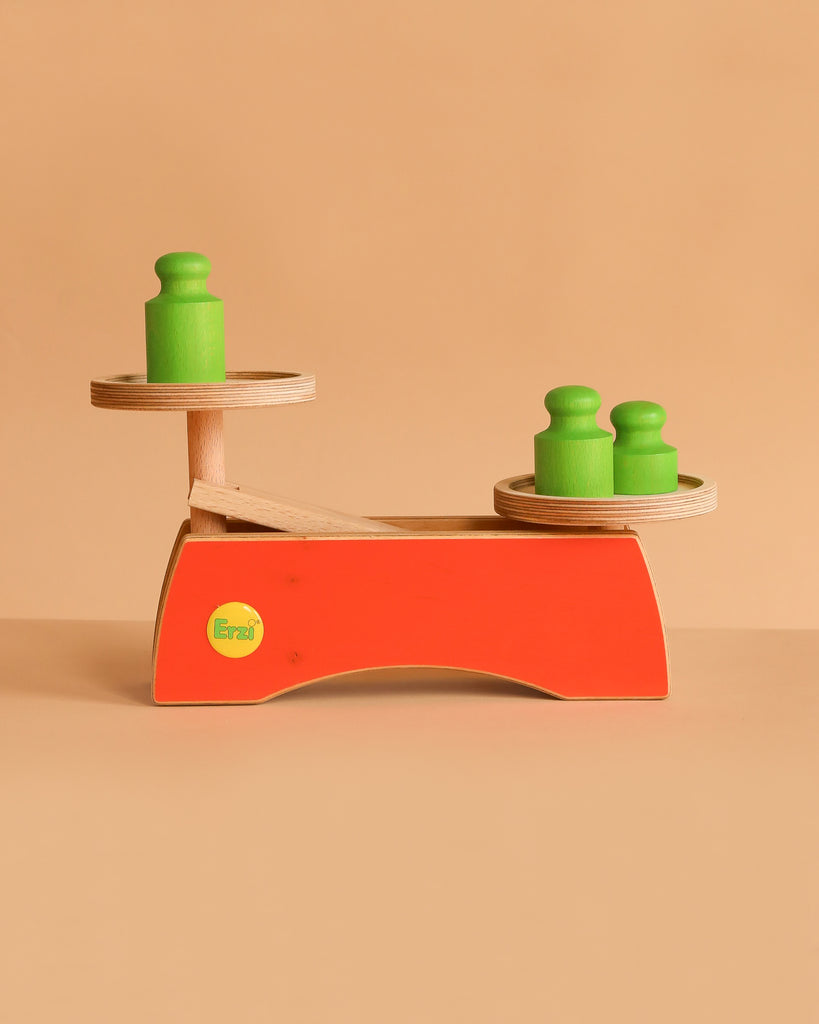 The Erzi Grocer's Scale For Pretend Food is a wooden children's weighing scale with an orange base, two trays, and green weights—ideal as an educational toy for little learners.