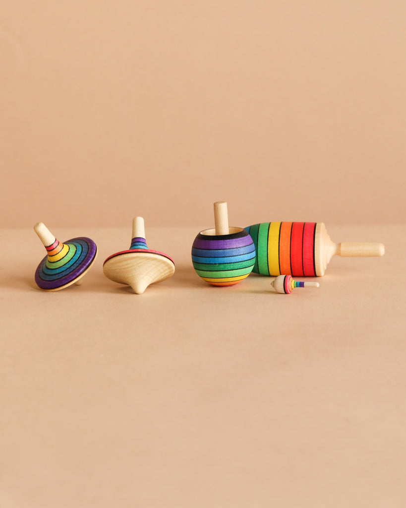 The Spinning Top Champion Learning Set - Rainbow features four vibrant tops of various shapes and sizes, each with bright rainbow stripes, all designed to meet toy safety standards for safe, enjoyable play.