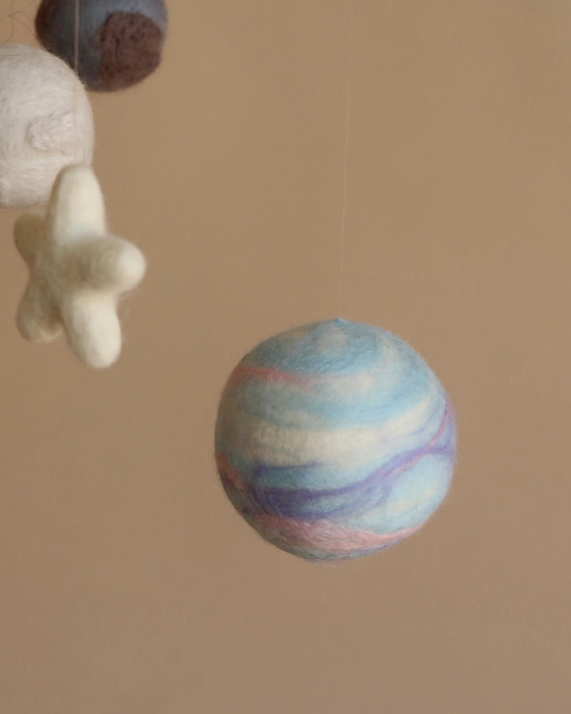 A close-up of a Handmade Mobile - Outer Space - Final Sale featuring a colorful planet with shades of blue, purple, and red, suspended against a soft beige background.