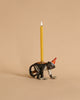 A whimsical Monkey Cake Topper shaped like a black monkey wearing a red party hat, with a lit beeswax birthday candle on its back against a beige background.