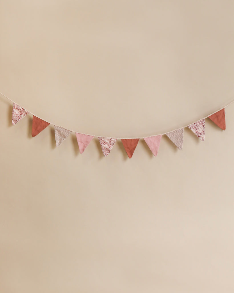 A Maileg garland in shades of pink and patterned gray, hung against a soft beige background.