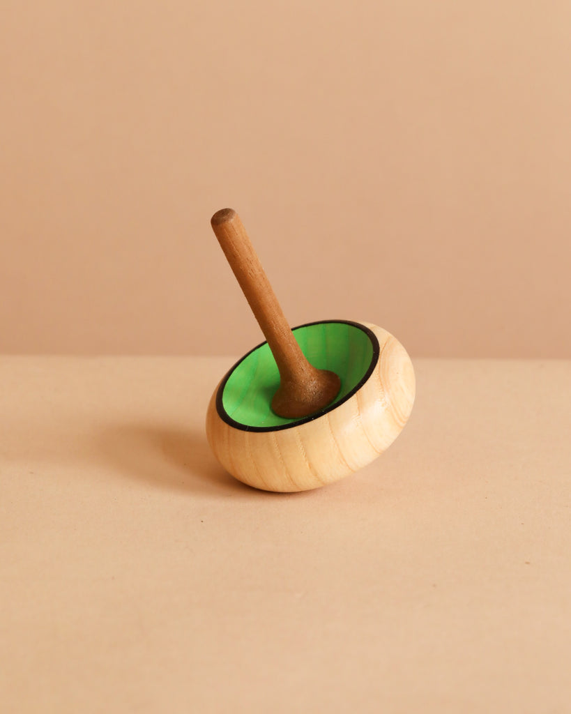 The Mader Zwirbel Spinning Top - Green, crafted from Walnut and Ash with a green inner circle, rests on its side against a plain beige background and meets toy safety standards.