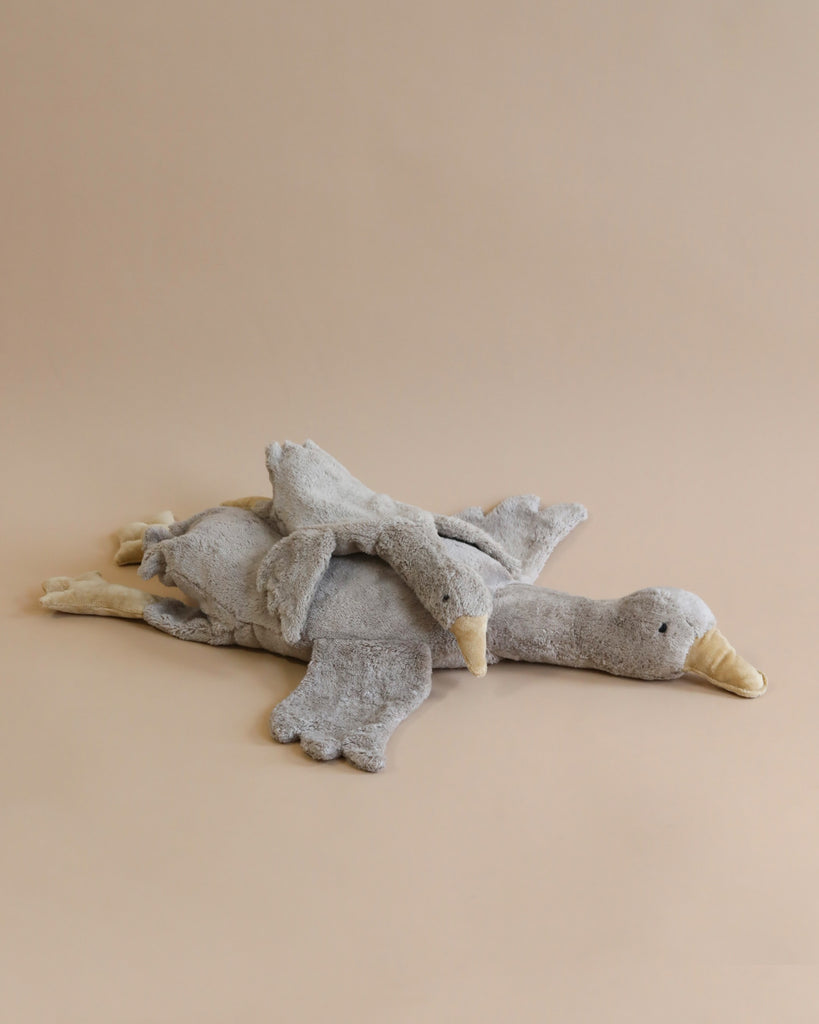 A Senger Naturwelt Cuddly Animal - Grey Goose, with a distressed texture, lying flat on a beige background. The toy has a neutral gray color with visible stitching and fabric textures, enhancing its lif