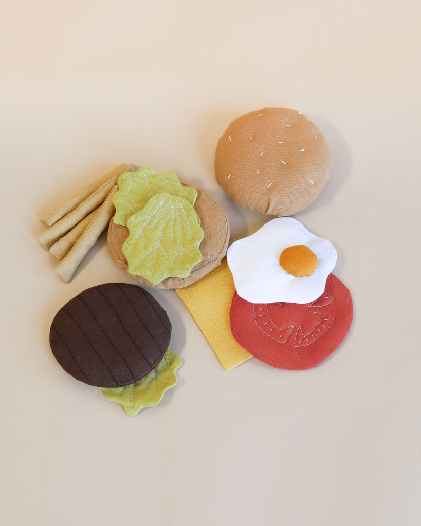 Various handmade soft cheeseburger and fries items including a burger with hamburger buns, and vegetables like lettuce and tomato, neatly arranged on a light beige background.