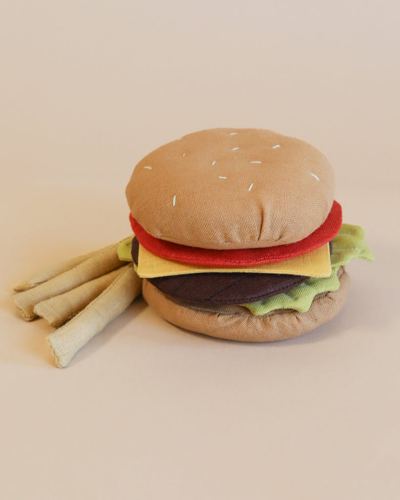 A handmade soft cheeseburger and fries shaped like a burger, featuring layers resembling hamburger buns, lettuce, tomato, cheese, and a patty, set against a pale background.