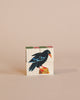 A colorful bird depicted on a Wooden Block Puzzle - Mini 4 Piece Domestic Animals made from sustainably harvested trees against a pale pink background. The bird is illustrated mid-motion, with vibrant blue and green feathers.