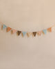 A string of Maileg Garland - Ocher flags in festive multi-colored shades of pink, blue, and brown hangs against a soft beige background.