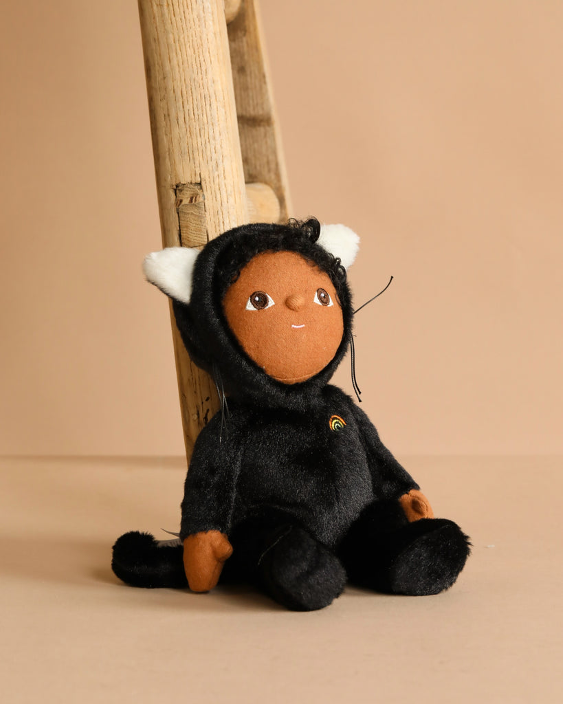 The Olli Ella Dinky Dinkum Doll - Carson Cat - Black features a plush doll with brown skin, large eyes, and a black cat velvet onesie—perfect as a Halloween soft toy for any space.