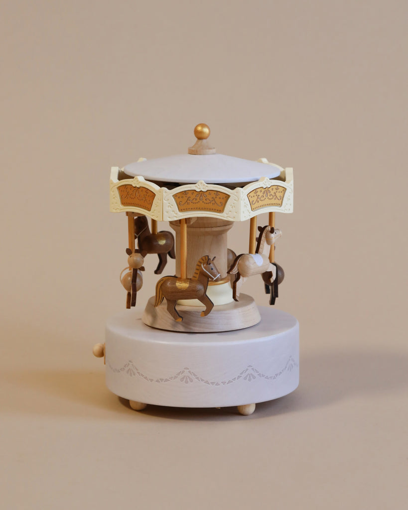 Wooden carousel music box with engravings gold detail. Six horses in dark brown and light brown going around the carouse.