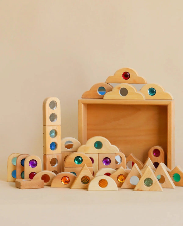 A collection of German quality toys, including the Bauspiel Fairytale Mixed Gemstone Set With Tray (36 pieces) wooden blocks and arches with colorful translucent gems, neatly arranged against a soft beige background.