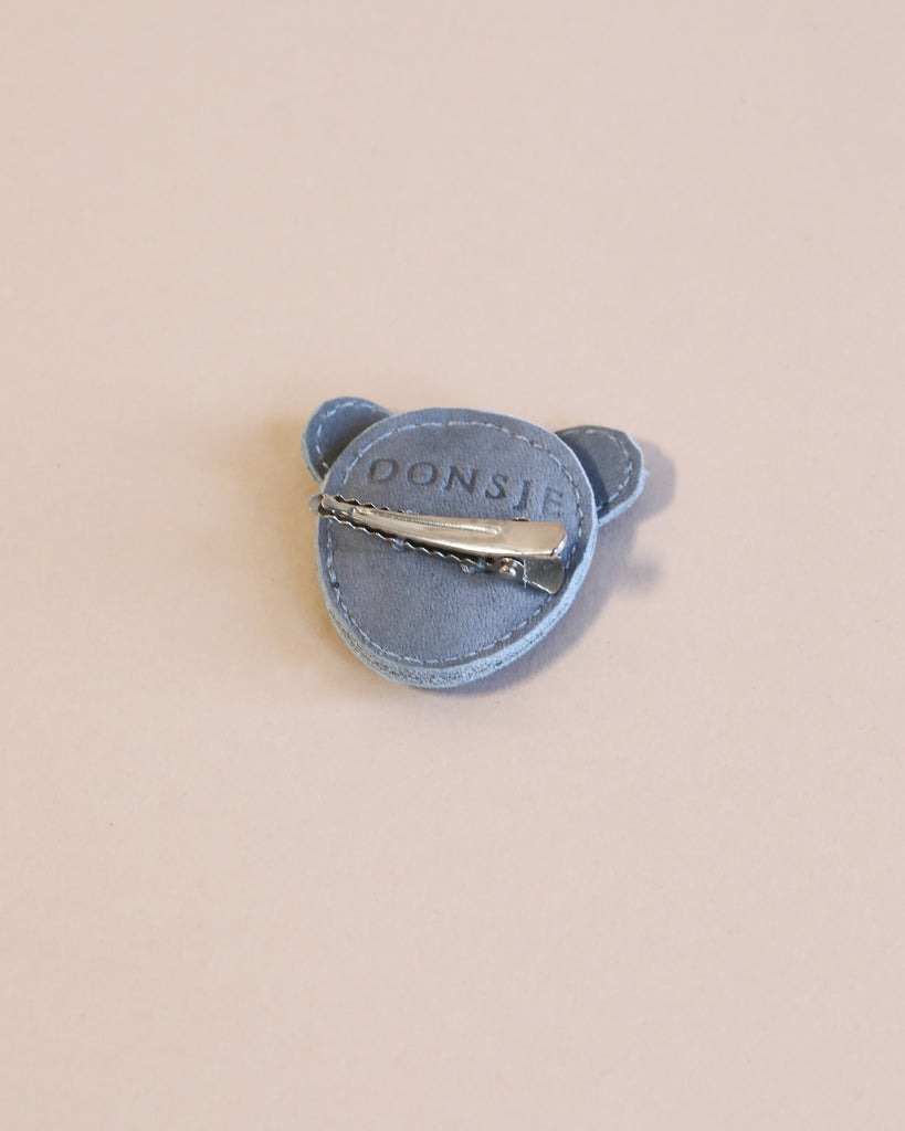 A Donsje Leather Hairclip - Mouse styled like a speech bubble, displaying the word "doors" in white letters, with a handmade fairtrade silver metal clip on the back, against a light beige.