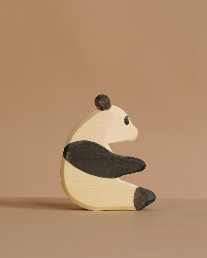 The Ostheimer Panda Bear, Sitting, is a small handcrafted wooden toy featuring painted black and white markings, shown upright on a plain beige surface with a matching background, highlighting Ostheimer's renowned quality.
